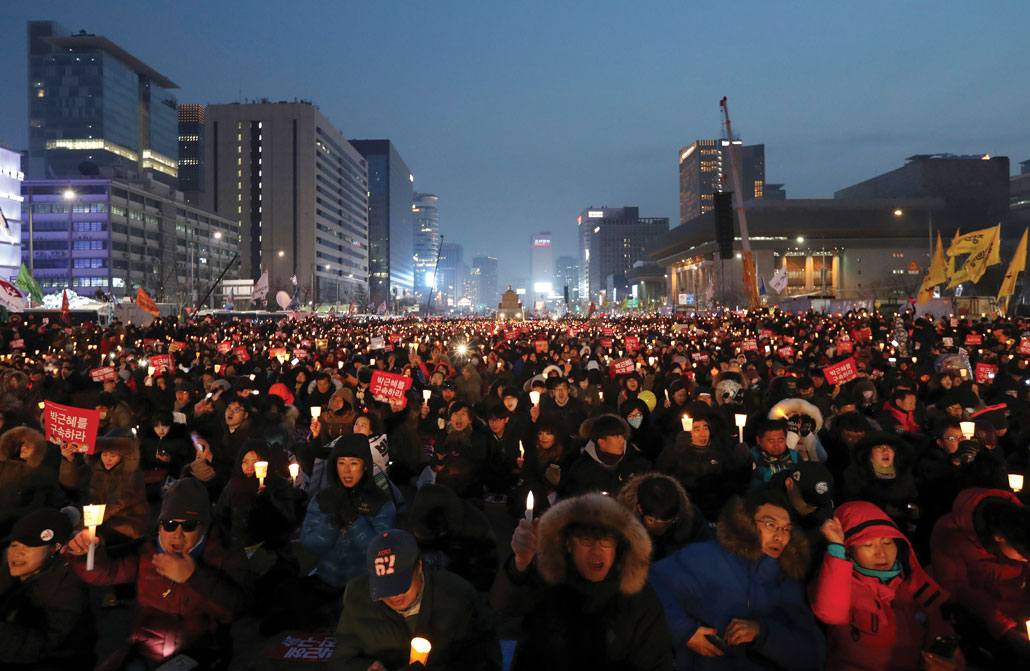 A photo of a large group of people outside in the winter holding signs and candles in protest.